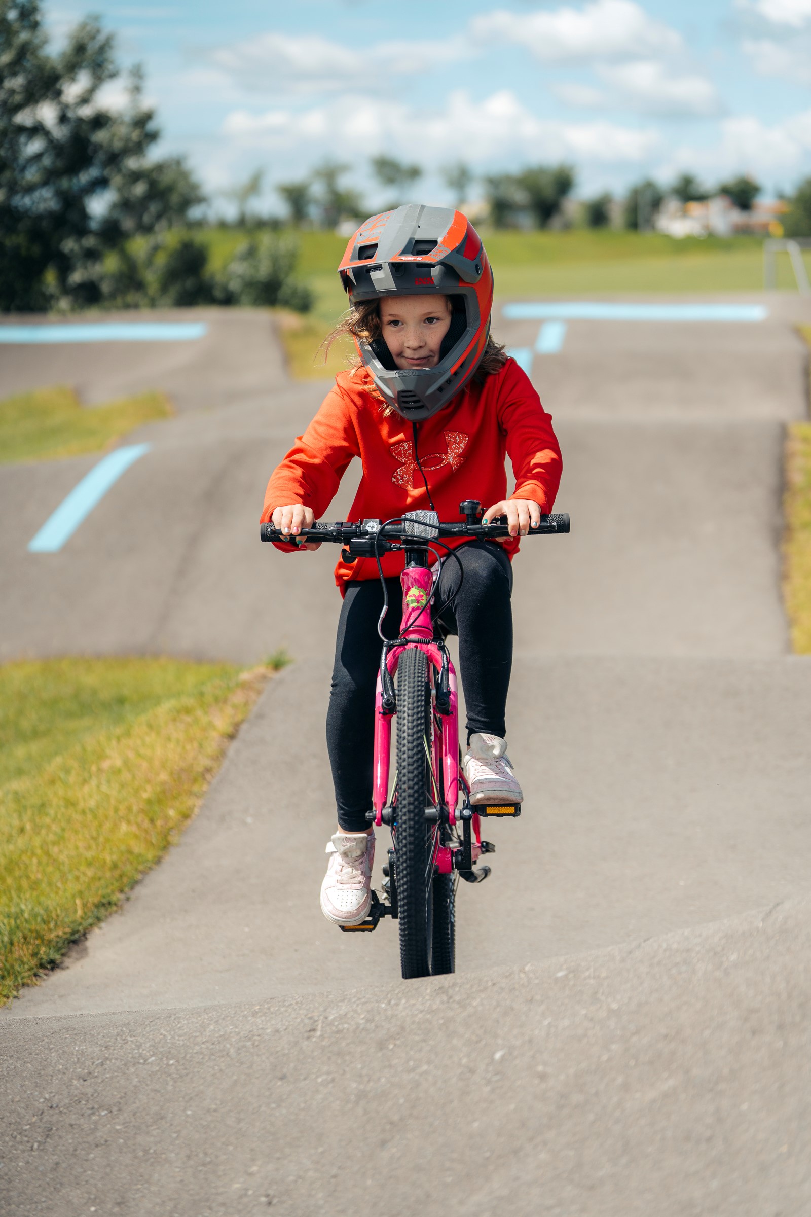 A kid riding a pink Frog 53 bike on a pumptrack