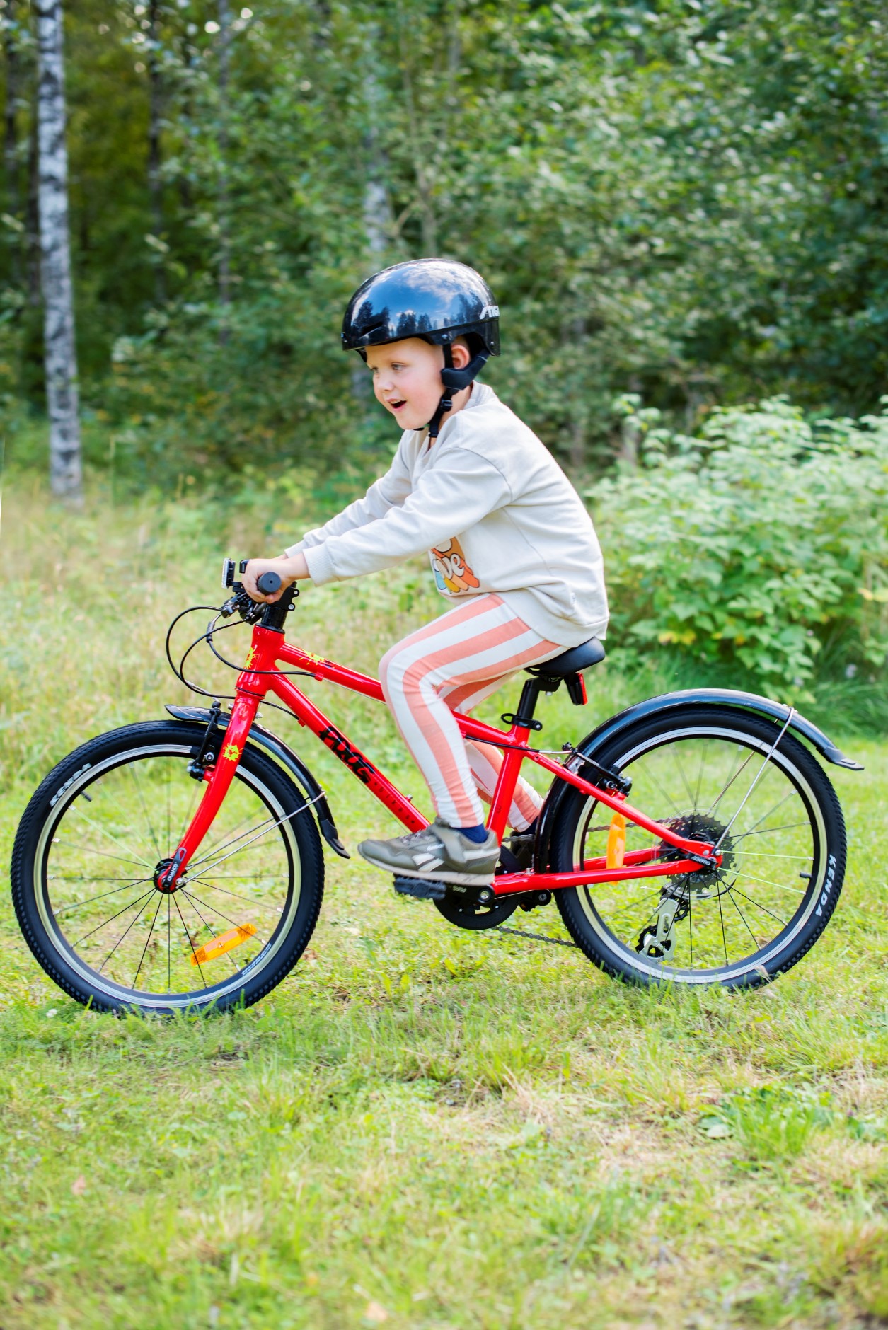 A kid riding a red Frog 53 bike on the grass