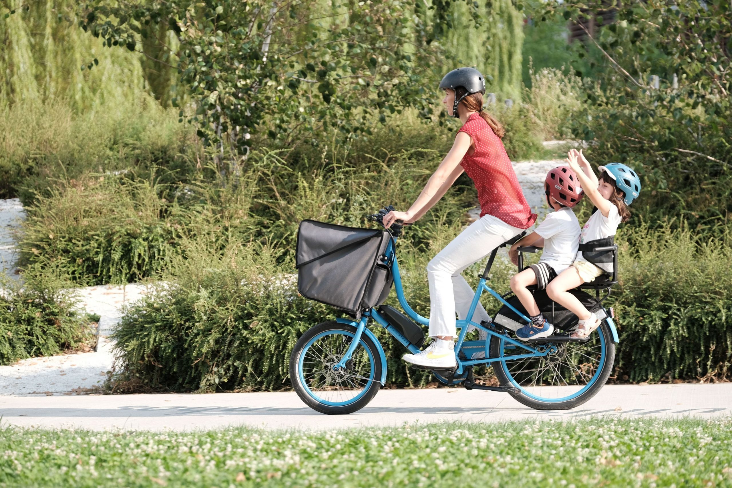 A woman with 2 children riding a Bicicapace Classicona cargo bike in a park
