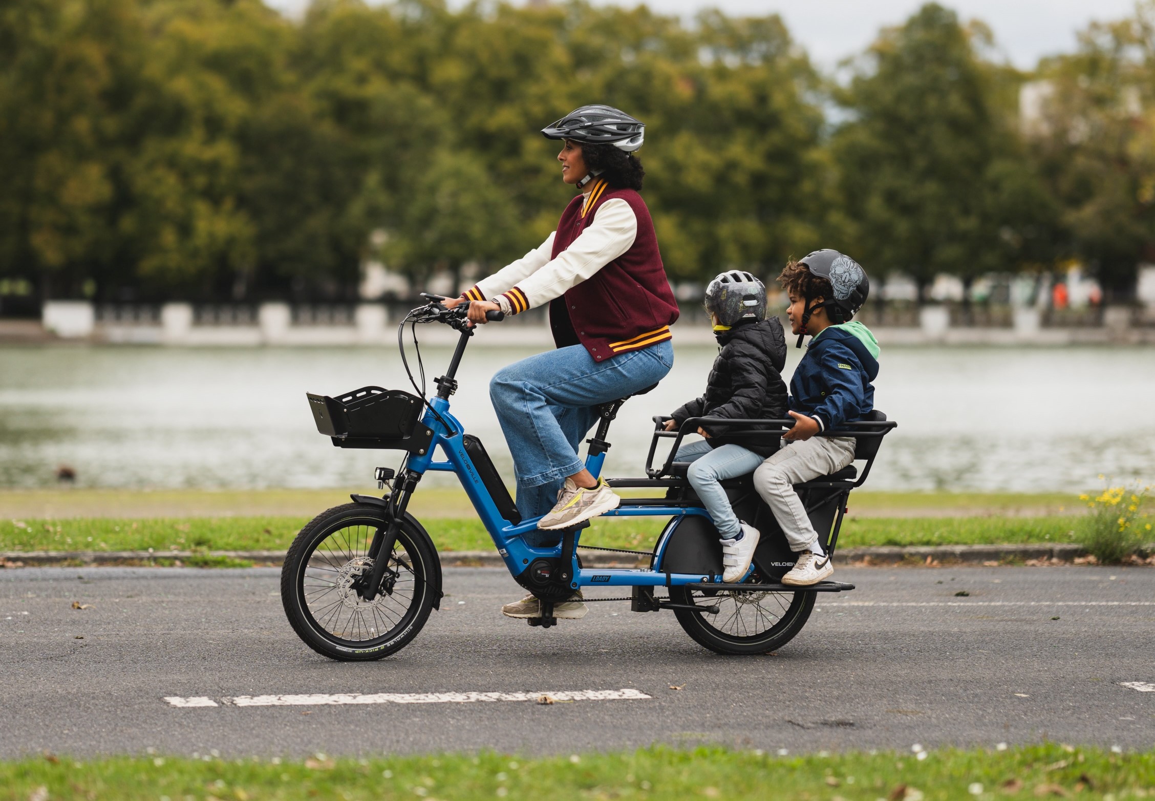 A woman riding a Velo De Ville Loady bike with two kids on the backseat