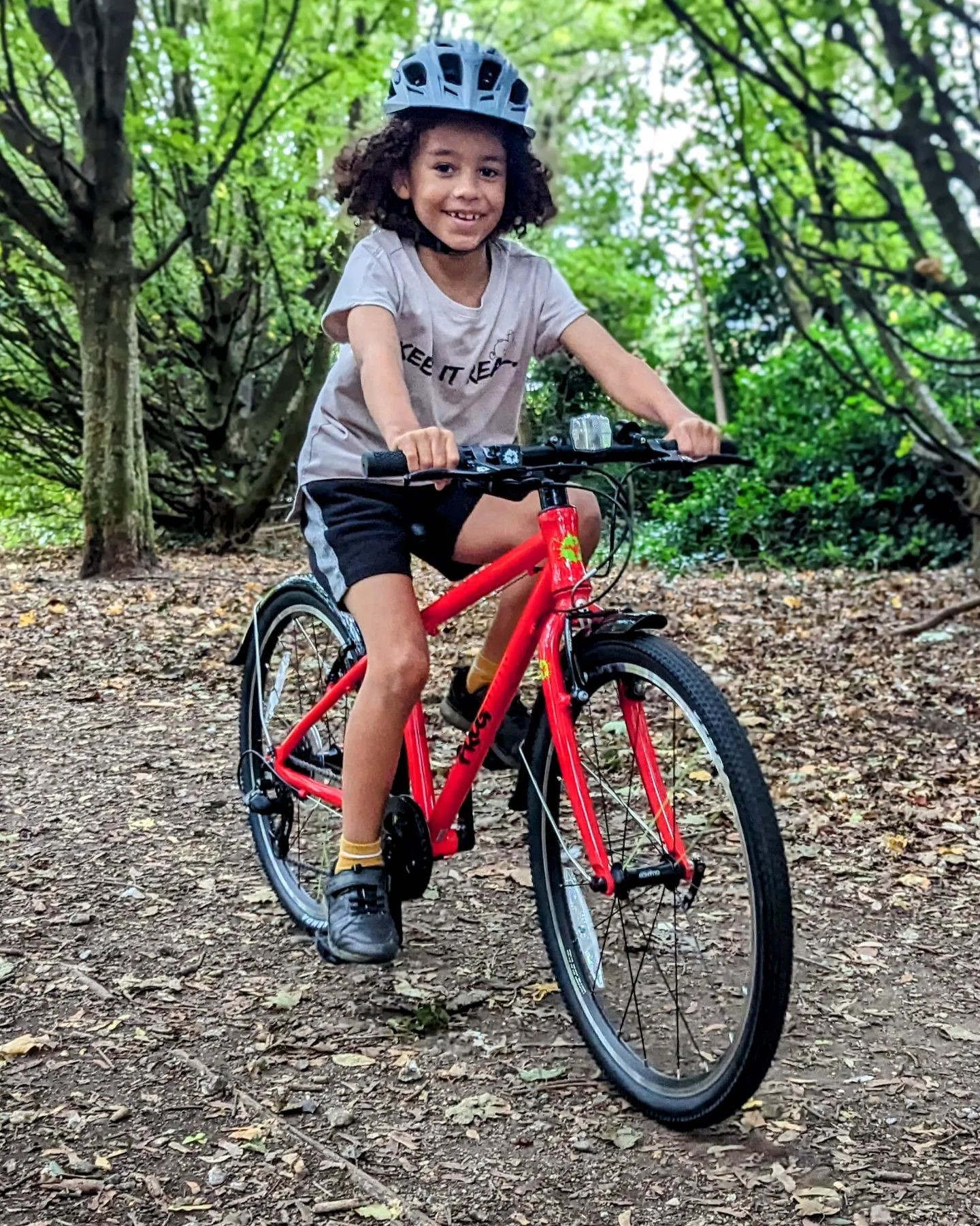 A kid sitting on a red Frog 61 bike in the woods