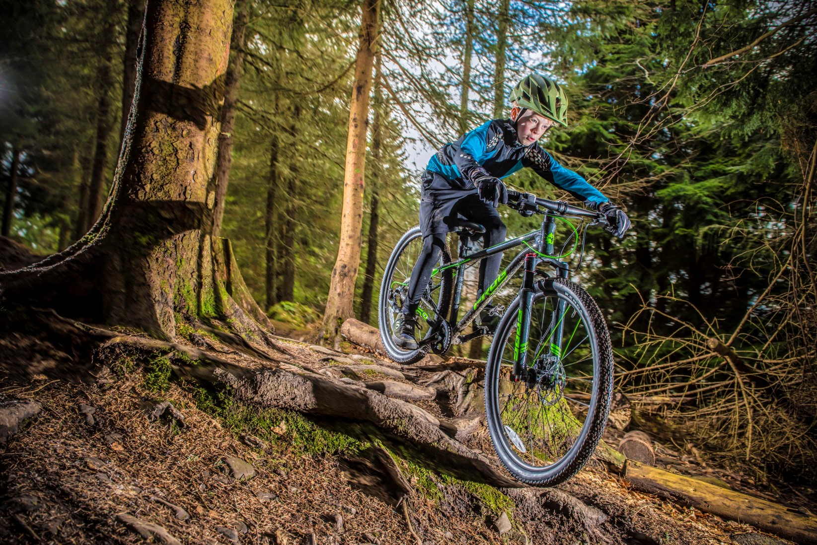 A boy riding on tree roots on a Frog Mountain 69 bike